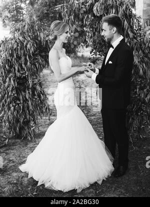 Matura in un abito da sposa anelli di scambi in giardino con un arco. foto in bianco e nero Foto Stock