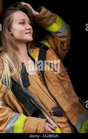 Immagine della giovane donna pompiere in tuta nera su sfondo vuoto in studio Foto Stock