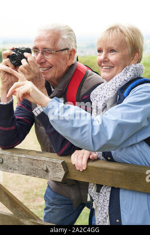 Coppia senior escursionismo in campagna in piedi da Gate e prendendo la foto con la fotocamera Foto Stock