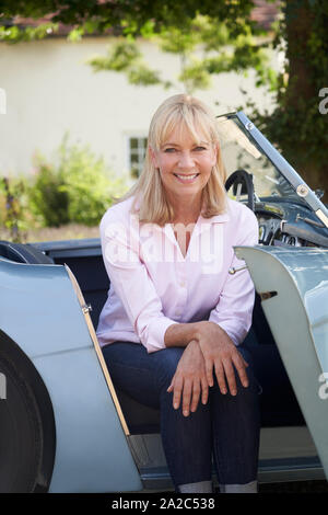 Ritratto di orgogliosa donna matura in seduta restaurato classico auto sportive all'aperto a casa Foto Stock
