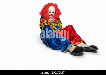 Triste clown seduto sul pavimento isolato sullo sfondo Foto Stock