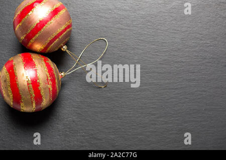 Due rosso e oro baubles di Natale al buio su un superficie di ardesia Foto Stock