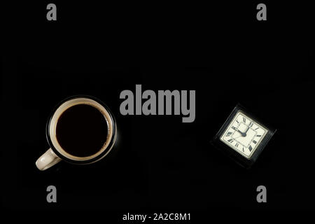 Mattina. Una tazza di caffè e un orologio da tavolo nero su sfondo isolato Foto Stock
