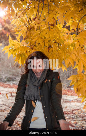 Bella giovane donna in una foresta di autunno gettando secchi di foglie di colore arancione e ridere Foto Stock