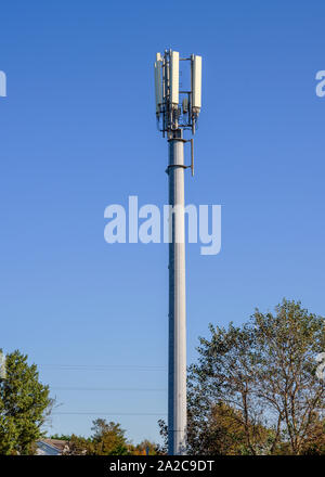 Telefono cellulare e montante di comunicazioni fotografati contro un luminoso cielo blu Foto Stock