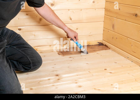 L'uomo le guarnizioni di tenuta di un pavimento in legno con uno smalto e un pennello Foto Stock