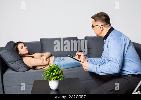 Giovane donna alla psicoterapeuta, sdraiato sul lettino, emotivamente, discutendo con la psicoterapeuta dei suoi problemi, praticante rendendo alcune note Foto Stock