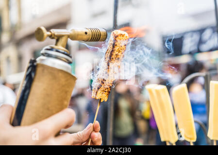 Un chef formaggio grill con un gas da cucina torcia presso un mercato alimentare. Foto Stock