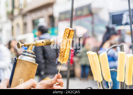 Un chef formaggio grill con un gas da cucina torcia presso un mercato alimentare. Foto Stock