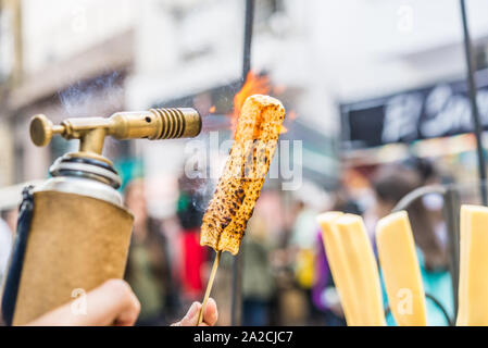 Un chef formaggio grill con un gas da cucina torcia presso un mercato alimentare. Foto Stock