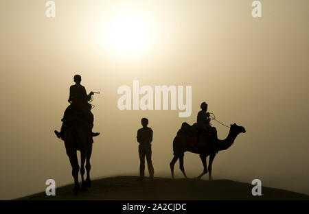 Tramonto nel deserto di Thar - silhouette di un ragazzo che sta in mezzo a piloti di cammello Foto Stock