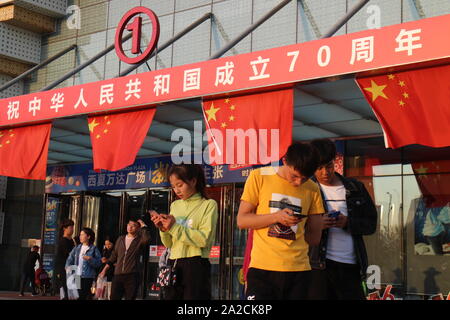 Yinchuan, Ningxia, Cina. Il 30 settembre, 2019. Un gruppo di adolescenti di utilizzare i loro telefoni cellulari nella parte anteriore di Wanda Plaza entrata principale decorato con le bandiere nazionali e lo slogan '' celebrazioni più caldi del settantesimo anniversario della fondazione della Repubblica popolare cinese''.Il primo ottobre 2019, Cina commemora il settantesimo compleanno della fondazione della Repubblica popolare cinese. Le manifestazioni sono state organizzate in tutto il paese, raggiungendo un livello senza precedenti di mobilitazione dello spazio pubblico con le bandiere nazionali e slogan patriottico visualizzati in ogni disposizione di porzioni del territorio. Questi Foto Stock