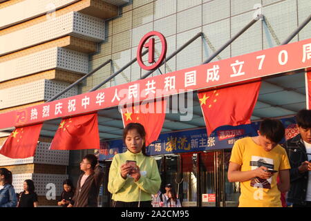 Yinchuan, Ningxia, Cina. Il 30 settembre, 2019. Un gruppo di adolescenti di utilizzare i loro telefoni cellulari nella parte anteriore di Wanda Plaza entrata principale decorato con le bandiere nazionali e lo slogan '' celebrazioni più caldi del settantesimo anniversario della fondazione della Repubblica popolare cinese''.Il primo ottobre 2019, Cina commemora il settantesimo compleanno della fondazione della Repubblica popolare cinese. Le manifestazioni sono state organizzate in tutto il paese, raggiungendo un livello senza precedenti di mobilitazione dello spazio pubblico con le bandiere nazionali e slogan patriottico visualizzati in ogni disposizione di porzioni del territorio. Questi Foto Stock