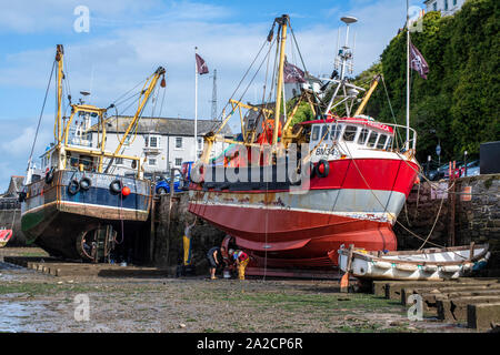 La Bassa marea a Brixham Harbour consente la possibilità per alcuni interventi di manutenzione per essere eseguita su scafi di un paio di sfogliare ormeggiata lungo la banchina Foto Stock