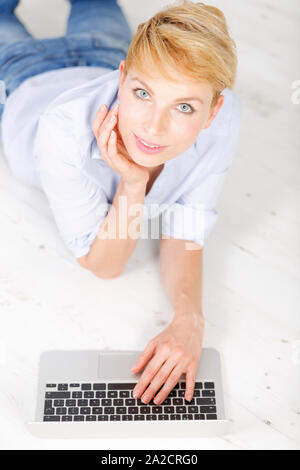 Attraente giovane donna con il suo computer portatile sdraiato sul pavimento Foto Stock