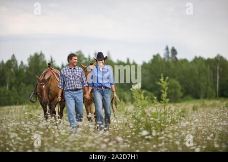 Coppia matura che portano i cavalli attraverso un prato Foto Stock