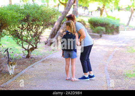 Street senzatetto cat. La nipote per mano di sua nonna ed essi guardando senzatetto kitty nel parco all'aperto. Ragazza e donna alimenta il abbandonato pet vagante sulla strada. Foto Stock