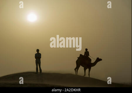 Tramonto nel deserto di Thar con ragazzo permanente e la silhouette di cammello Foto Stock