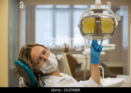 Una femmina di dentista in bicchieri e una Benda di garza si siede in un riunito dentale. Foto Stock