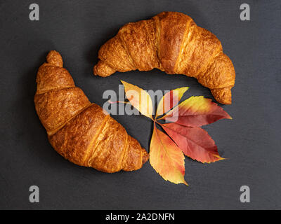 Croissant sul grigio scuro dello sfondo in ardesia con foglie di autunno. Minimal design concept. Foto Stock