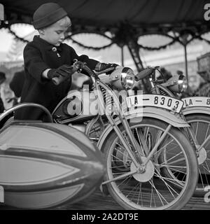 Ein kleiner Junge auf dem Motorrad eines Kinderkarussels auf dem Weihnachtsmarkt, Deutschland 1930er Jahre. Un ragazzino in sella alla moto di una giostra kiddy presso il mercato di natale, Germania 1930s. Foto Stock