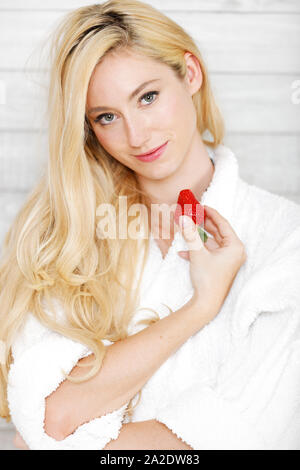 Bella giovane donna in una veste bianca godendo di una fragola fresca Foto Stock
