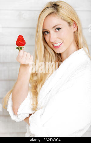 Bella giovane donna in una veste bianca godendo di una fragola fresca Foto Stock
