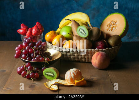 ancora frutti di vita su un tavolo di legno, uva fragole kiwis pesca melon banana mandarino sbucciato Foto Stock