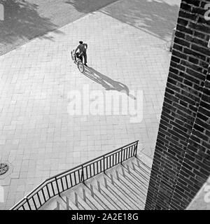 Impressione aus Düsseldorf: ein Mann steht mit seinem Fahrrad auf einem Platz vor einem Backsteingebäude, 1930er Jahre. Impressione Da Duesseldorf: un uomo in piedi con la sua bicicletta su una piazza di fronte ad un edificio, 1930s. Foto Stock