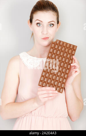 Attraente giovane donna di decidere se andare a mangiare un pezzo di cioccolato. Foto Stock