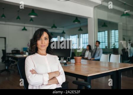 Sorridente giovane imprenditrice seduto alla sua scrivania nel pomeriggio Foto Stock