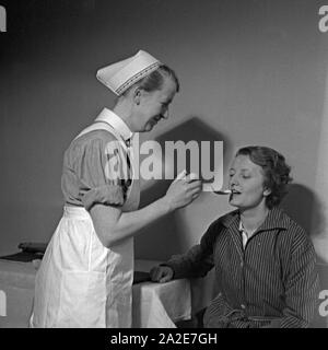 Eine Schwester des Deutschen Roten Kreuzes verarbreicht einer Kranken einen Löffel Medizin, Deutschland 1930er Jahre. Un nburse della Croce Rossa tedesca applicando alcune medicine per una donna malata, Germania 1930s. Foto Stock