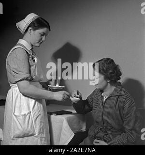 Eine junge Schwester des Deutschen Roten Kreuzes verarbreicht einer Kranken eine Tablette, Deutschland 1930er Jahre. Un giovane infermiere della Croce Rossa tedesca applicando una pillola per una donna malata, Germania 1930s. Foto Stock