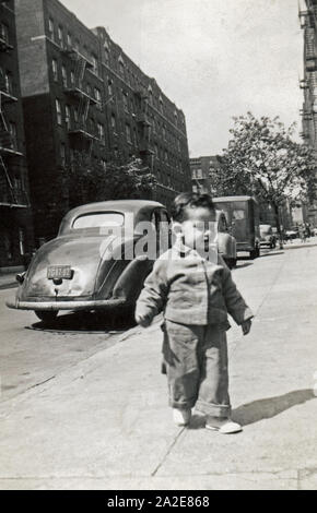 Il Toddler boy camminando lungo il marciapiede in un urbano per la città di New York, Stati Uniti, circa 1949. Foto Stock