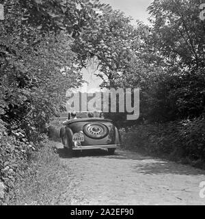 Werbefoto für den Personenkraftwagen Ford Eifel Mit einem Paar bei einer Fahrt durch den Wald, Deutschland 1935. Fotografia commerciale per le automobili Ford Eifel con coppia di guida attraverso una foresta, Germania 1935. Foto Stock