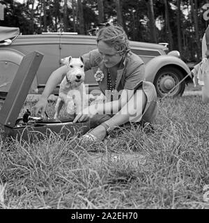 Eine junge Frau und ein Foxterrier sitzen in der Wiese bei einem Electrola Koffer 106 Grammophon, Deutschland 1930er Jahre. Una giovane donna e un fox terrier seduto su un prato da un Electrola Koffer 106 valigia gramophone, Germania 1930s. Foto Stock