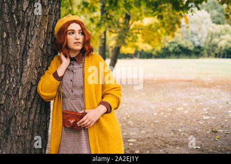 Una bella rossa dai capelli donna con una pettinatura ricci è in piedi nel parco Foto Stock