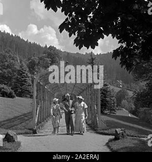 Ein Mann spaziert mit zwei Frauen durch ein Rankgerüst in Wildbad im Schwarzwald, Deutschland 1930er. Due donne e un uomo passeggiando attraverso un pergolato a Wildbad nella Foresta Nera, Germania 1930s. Foto Stock