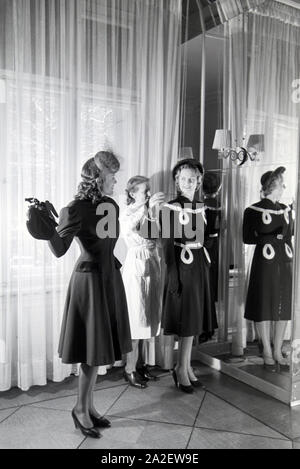 Modelli Zwei und eine Schneiderin bei der Anprobe von Kleidern von Modeschöpferin Annemaria Geise; Deutschland ca. 1939. Due modelli e un sarto cercando abiti dei designer di moda Annemaria Geise; Germania ca. 1939. Foto Stock