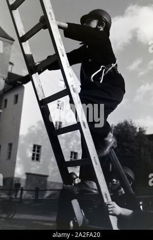 Ein Junge von der Kinderfeuerwehr erklettert bei einer Feuerwehrübung eine Leiter, Deutschland 1930er Jahre. Un ragazzo della junior vigili del fuoco è salire una scala a pioli durante un vigile del fuoco di formazione, Germania 1930s. Foto Stock