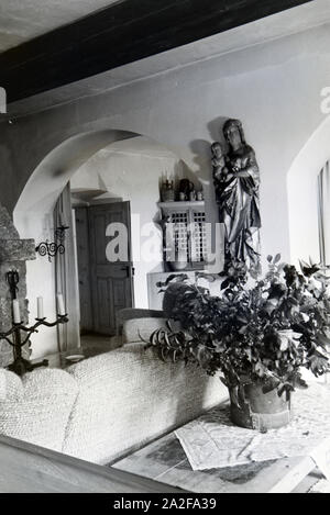 Wohnraum mit Polstermöbeln und einer Skulptur der Heiligen Maria mit Jesuskind auf Schloss Hartmannsberg, dem Wohnsitz von Bildhauer Josef Thorak, Deutschland 1930er Jahre. Salotto con tappezzeria e una scultura di Santa Maria e il Bambino Gesù nel castello di Hartmannsberg, la residenza dello scultore Josef Thorak, Germania 1930s. Foto Stock