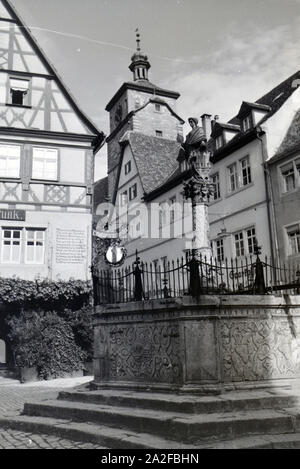 Ein Springbrunnen mit einer kleinen statua in Rothenburg ob der Tauber, von der dem gotische Teil mitsamt hohem Turm im Hintergrund sichtbar Ist Deutschland 1930er Jahre. Una fontana con una piccola statua in Rothenburg ob der Tauber, con il gotico e la parte alta towerin sullo sfondo, Germania 1930s. Foto Stock