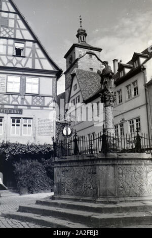 Ein Springbrunnen mit einer kleinen statua in Rothenburg ob der Tauber, von der dem gotische Teil mitsamt hohem Turm im Hintergrund sichtbar Ist Deutschland 1930er Jahre. Una fontana con una piccola statua in Rothenburg ob der Tauber, con il gotico e la parte alta towerin sullo sfondo, Germania 1930s. Foto Stock