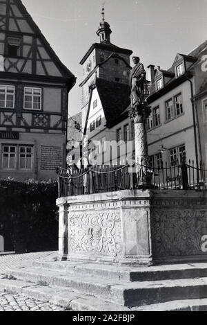 Ein Springbrunnen mit einer kleinen statua in Rothenburg ob der Tauber, von der dem gotische Teil mitsamt hohem Turm im Hintergrund sichtbar Ist Deutschland 1930er Jahre. Una fontana con una piccola statua in Rothenburg ob der Tauber, con il gotico e la parte alta towerin sullo sfondo, Germania 1930s. Foto Stock