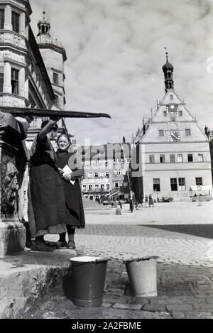 Zwei Frauen unterhalten sich während Sie die Wassereimer mit Wasser aus dem Springbrunnen Am Marktplatz vor dem Rathaus und der Ratstrinkstube voll laufen lassen, Rothenburg ob der Tauber, Deutschland 1930er Jahre. Due donne aventi una chat mentre il bucktes sono il riempimento con acqua dalla fontana posta nella piazza del mercato vicino al municipio e Ratstrinkstube a Rothenburg ob der Tauber, Germania 1930s. Foto Stock
