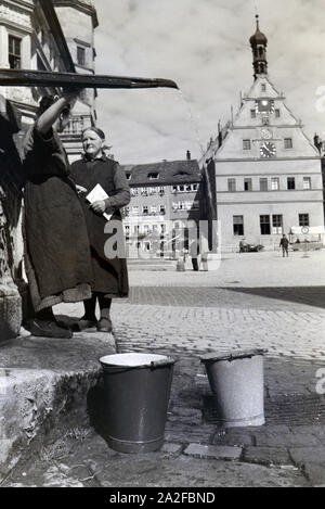Zwei Frauen unterhalten sich während Sie die Wassereimer mit Wasser aus dem Springbrunnen Am Marktplatz vor dem Rathaus und der Ratstrinkstube voll laufen lassen, Rothenburg ob der Tauber, Deutschland 1930er Jahre. Due donne aventi una chat mentre il bucktes sono il riempimento con acqua dalla fontana posta nella piazza del mercato vicino al municipio e Ratstrinkstube a Rothenburg ob der Tauber, Germania 1930s. Foto Stock