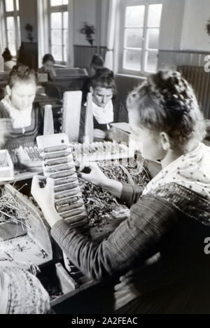 Eine Zigarrenrollerin in Marburger Tracht bei der Arbeit in einer Zigarrenfabrik bei Marburg, Deutschland 1930er Jahre. Una femmina di sigaro a rulli che indossa un abito di Marburg / costume di lavorare in un tessuto di sigaro vicino a Marburg, Germania 1930s. Foto Stock