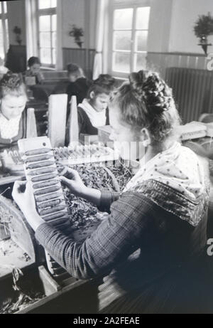 Eine Zigarrenrollerin in Marburger Tracht bei der Arbeit in einer Zigarrenfabrik bei Marburg, Deutschland 1930er Jahre. Una femmina di sigaro a rulli che indossa un abito di Marburg / costume di lavorare in un tessuto di sigaro vicino a Marburg, Germania 1930s. Foto Stock