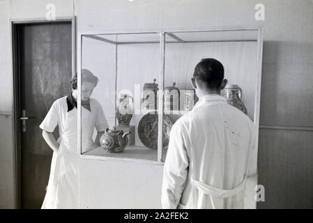 Zwei Schüler der Fachschule für Keramik in Höhr-Grenzhausen betrachten die ausgestellte Töpferware im Flur der Schule, Deutschland 1930er Jahre. Due studenti del Collegio per la Ceramica di Höhr-Grenzhausen guardando la ceramica esposti nel corridoio della scuola, Germania 1930s. Foto Stock