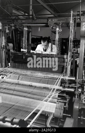 Ein Angestellter einer Textilfirma in Krefeld justiert das Garn in der großen Webmaschine, Deutschland 1930er Jahre. Un dipendente in una azienda tessile in Krefeld regolando il filo in una grande potenza telaio, Germania 1930s. Foto Stock
